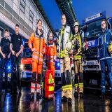 Rettungskräfte und Polizei stehen vor Einsatzfahrzeugen mit eingeschaltetem Blaulicht.